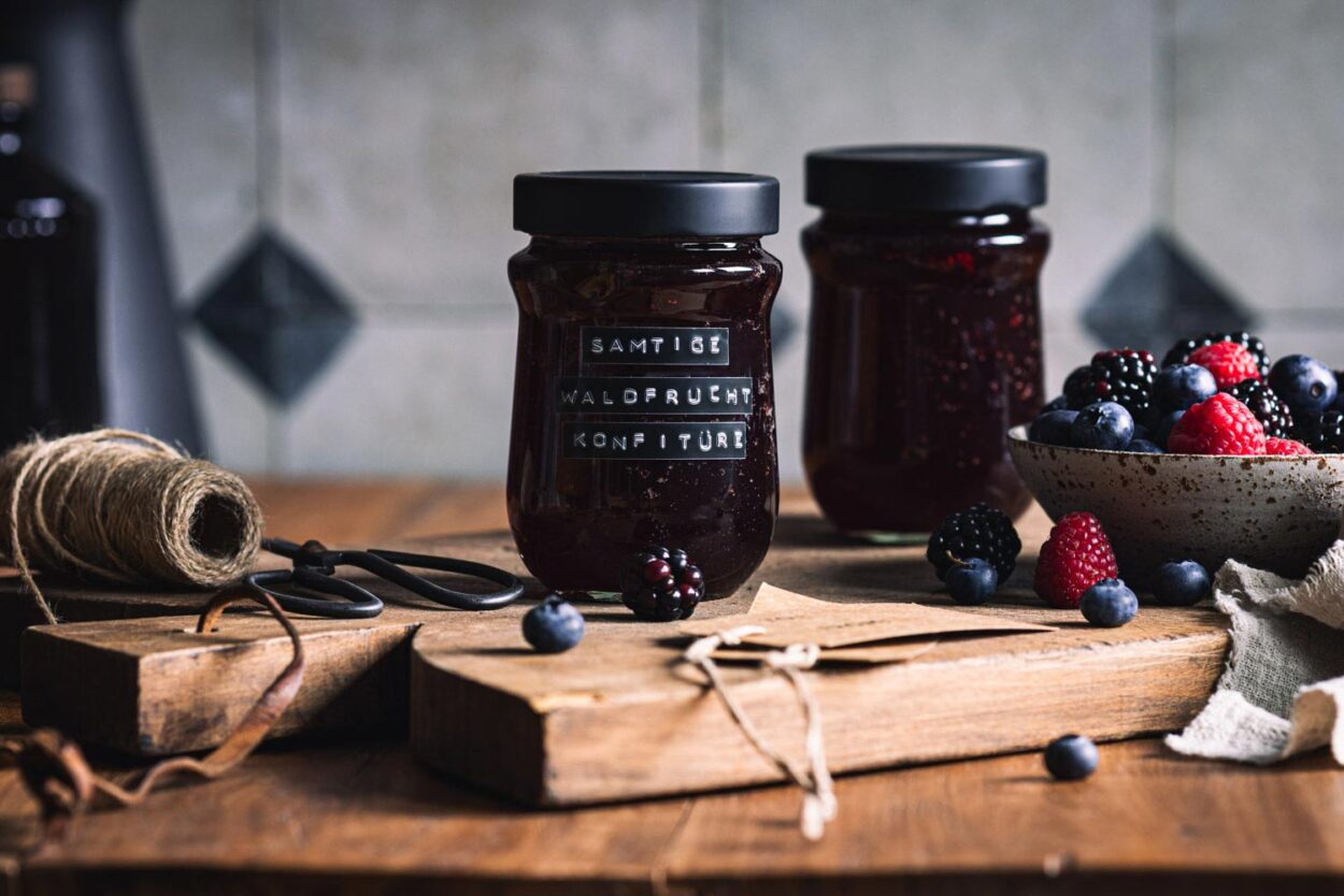 Waldfrucht Marmelade ohne Kerne in zwei Gläsern auf einem Holzbrett mit Beeren  im Hintergrund.