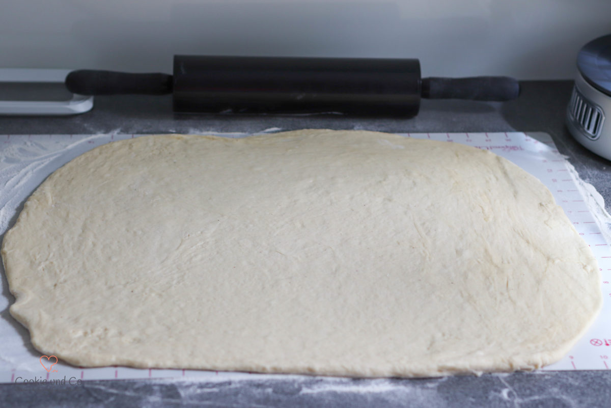 Ausgerollter Hefeteig für Blaubeer-Hefeschnecken auf einer Silikonunterlage mit einem Nudelholz im Hintergrund.