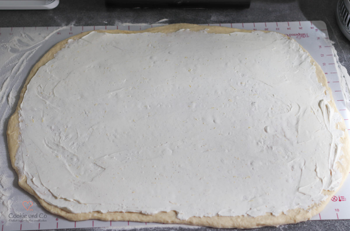 Ausgerollter Hefeteig für Hefeschnecken mit der verstrichenen Cheesecakefüllung.