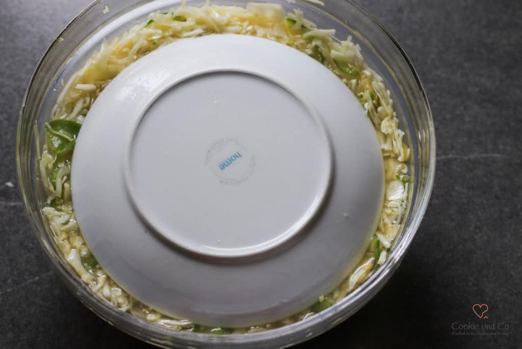 Weißkrautsalat in einer Glasschüssel mit einem Teller abgedeckt.