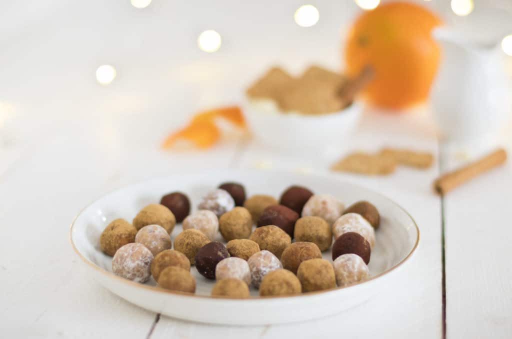 Spekulatius-Orangen-Konfekt auf einem weißen Teller mit einer Orange und Zimtstangen im Hintegrund. 