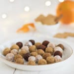 Spekulatius-Orangen-Konfekt auf einem weißen Teller mit einer Orange und Zimtstangen im Hintegrrund.