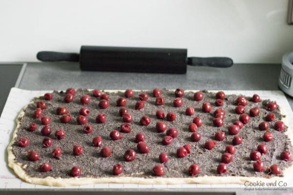 Ausgerollter Teig mit Mohnfüllung und Kirschen für Mohn-Schnecken mit Marzipan.