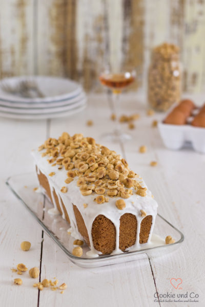 Nusskuchen, dekoriert mit Zucker und Haselnüssen auf einer Kuchenplatte.