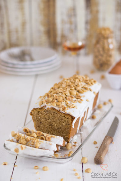 Nusskuchen, dekoriert mit Zucker und Haselnüssen auf einer Kuchenplatte.