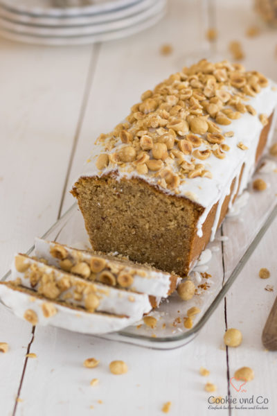 Nusskuchen, dekoriert mit Zucker und Haselnüssen auf einer Kuchenplatte.