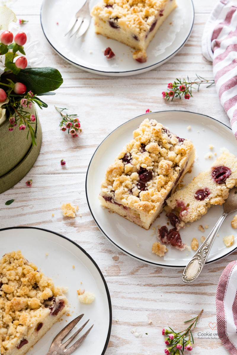 Kirschkuchen mit Streusel verteilt auf einem Tellern und Blumen im Hintergrund (schneller Blechkuchen aus Rührteig)