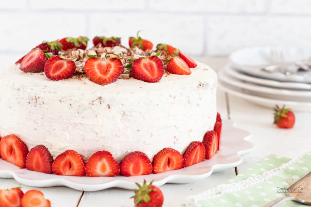 Erdbeertorte mit Yogurette auf einem Teller mit Kuchentellern im Hintergrund.