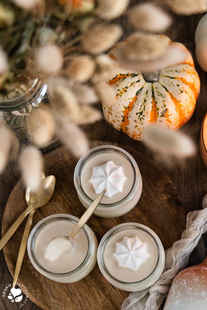 Weiße Schoko-Panna Cotta mit Likör auf einem Holzteller und einem Kürbis im Hintergrund.