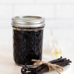 Selbst gemachter Vanilleextrakt in einem Einmachglas mit Vanilleschoten und einer Orchideenblüte daneben.