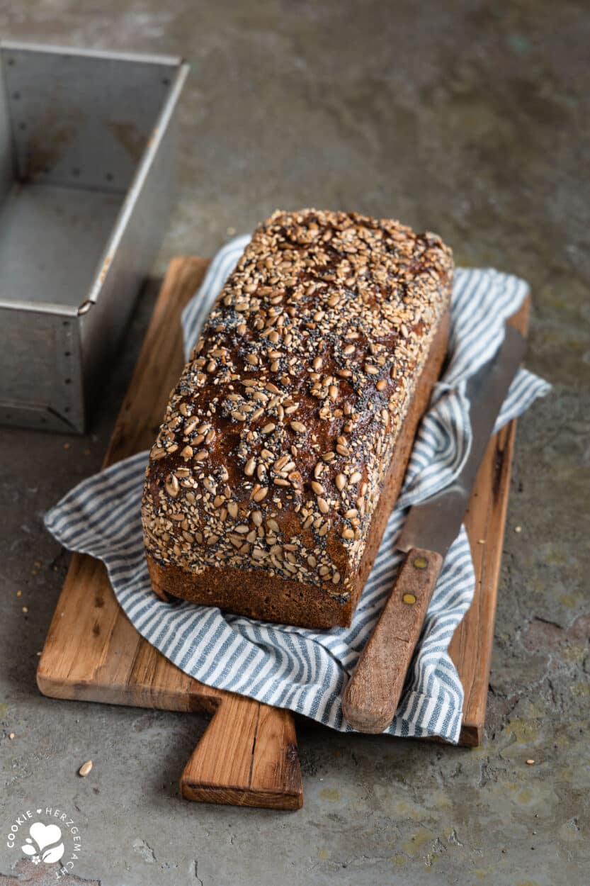 Dinkel-Saatling auf einem Holzbrett mit einem blau gestreiften Tuch darunter und einer Backform im Hintergrund.