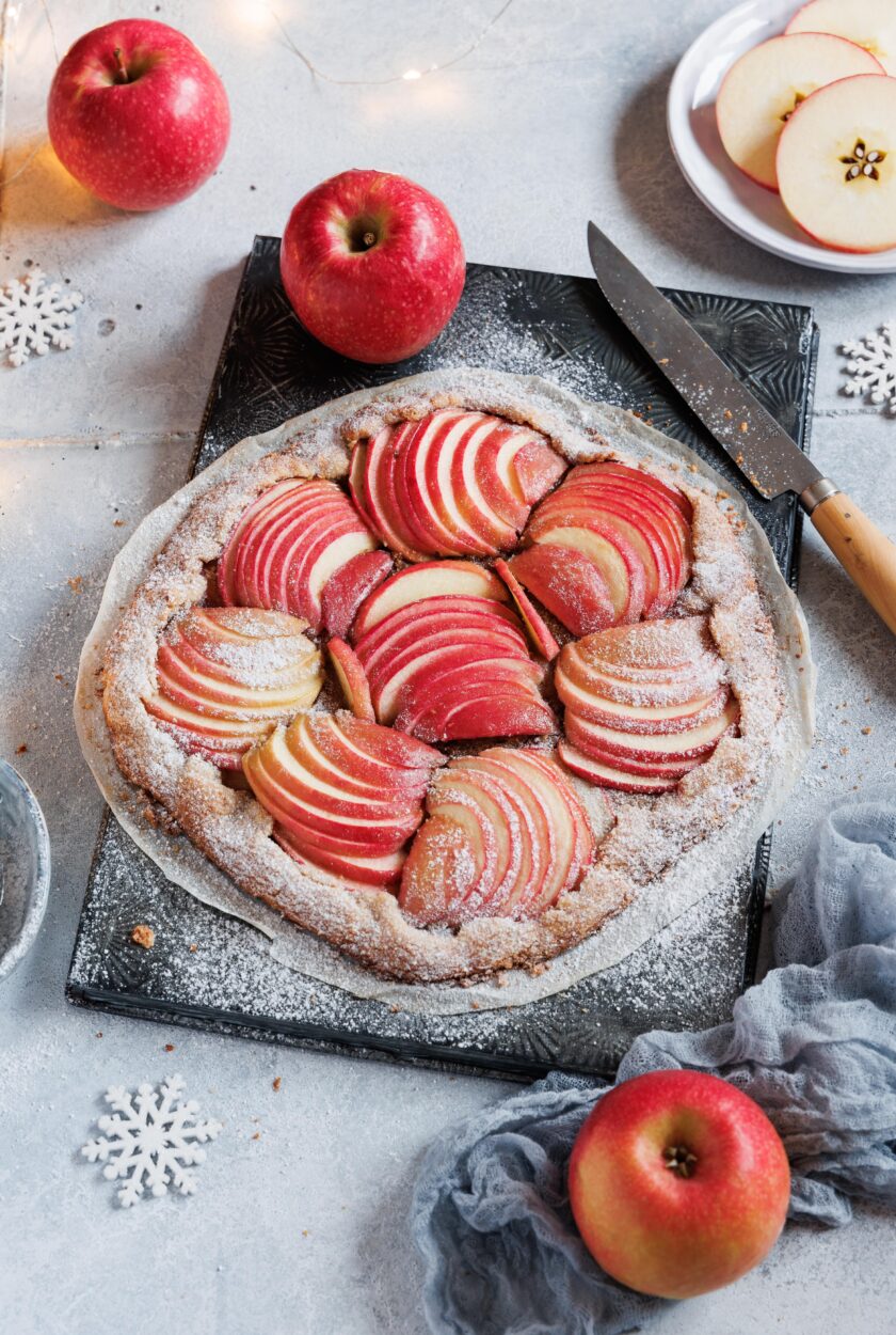 Eine Apfelgalette auf einem Backblech mit Äpfeln im Hintergrund.