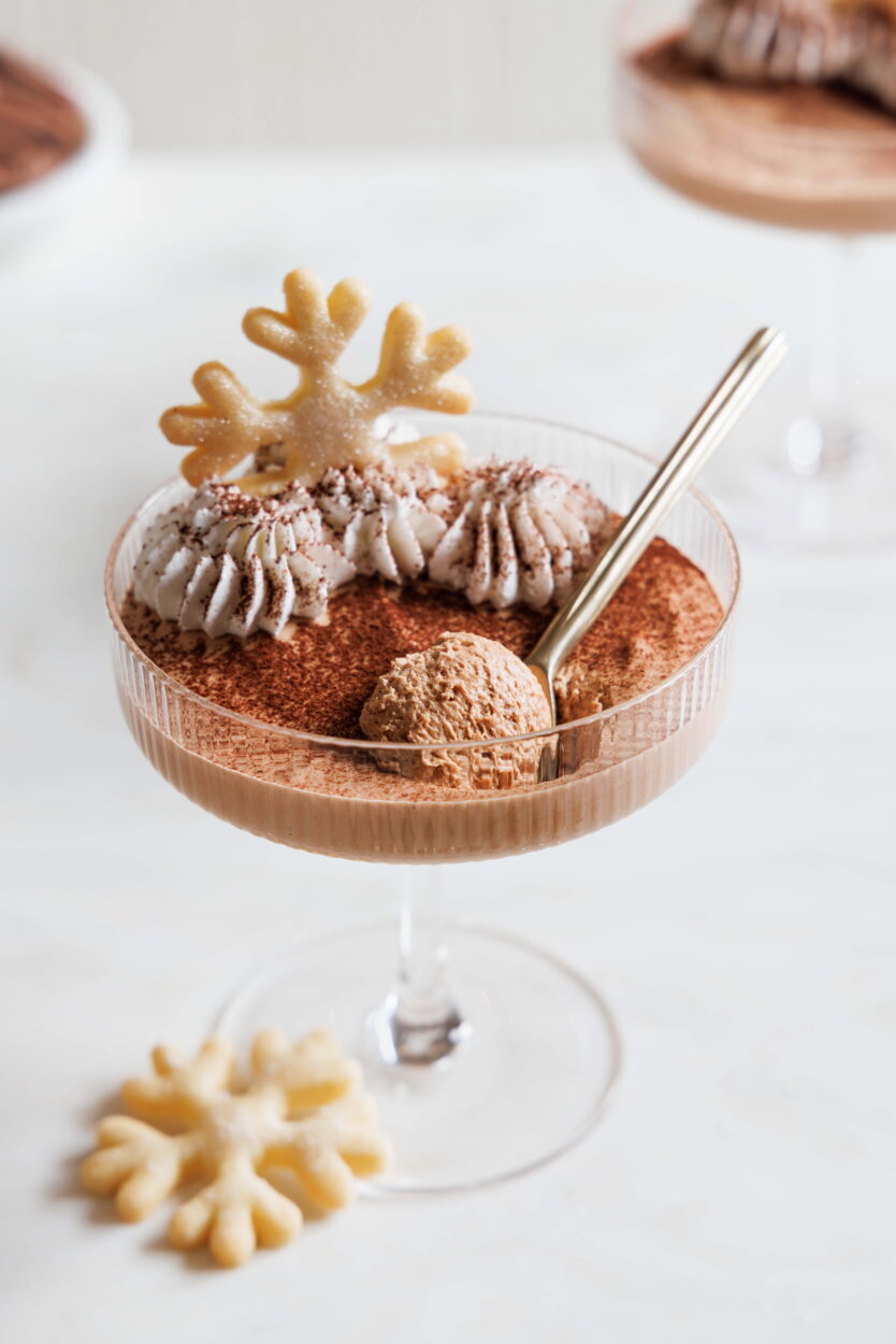 Baileysmousse in einem Champagnerglas, mit Sahne, Kakao und einem Plätzen n Schneeflockenform dekoriert.