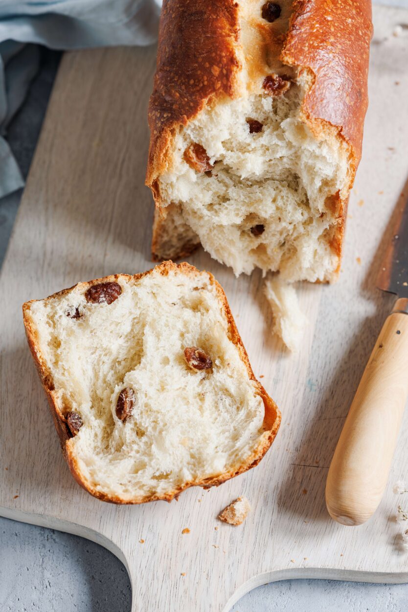 Nahaufnahme von einem Rosinenbrot, das aufgeschnitten auf einem Holzbrett mit einem Messer daneben liegt.