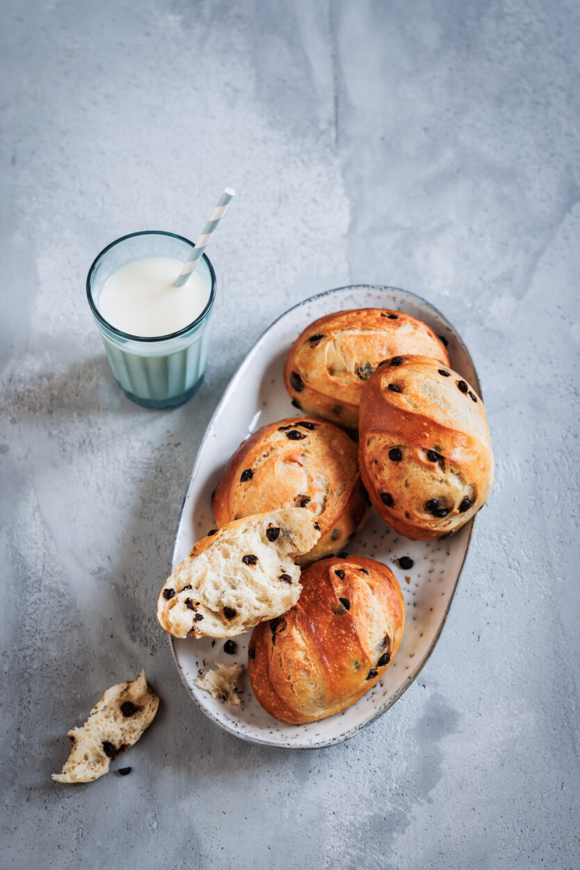 Milchbrötchen mit Schokoladenstücken auf einer Servierplatte mit einem Glas Milch daneben. 