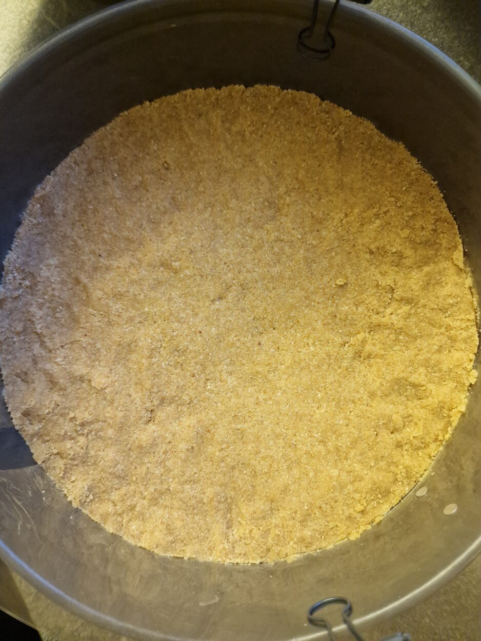 Festgedrückter Keksboden in einer Springform für einen Cheesecake.