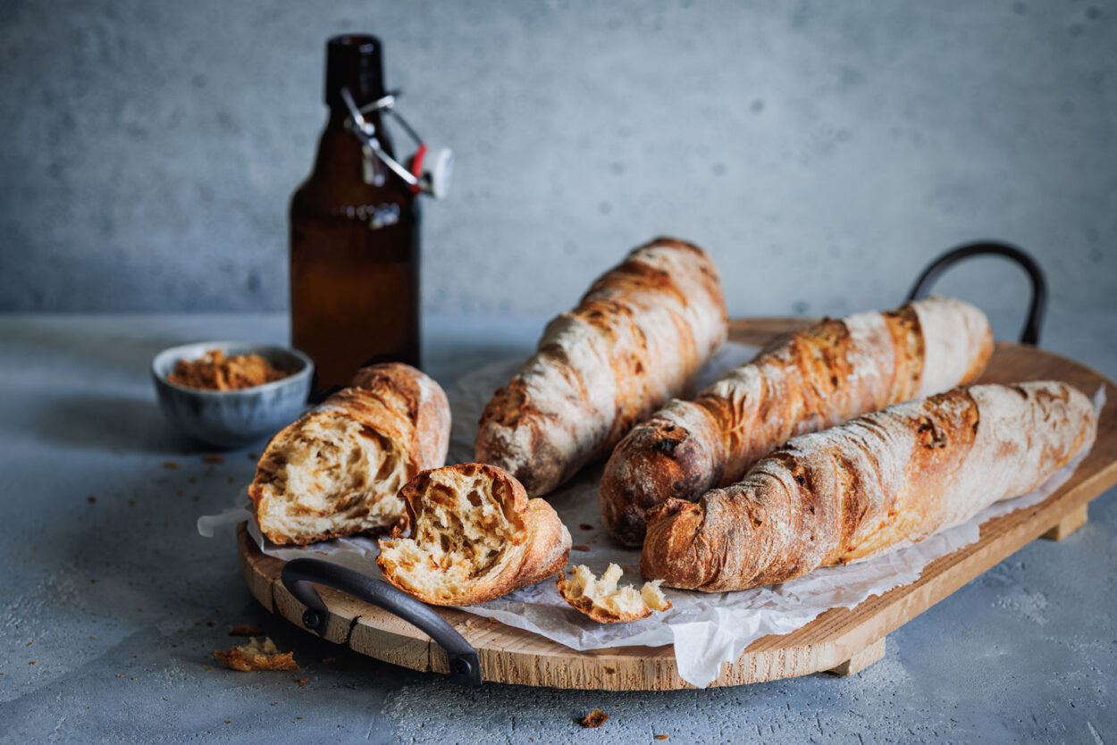 Zwiebel-Wurzelbrot auf einem rustikalen Holzbrett mit einer Flasche Bier und einem Schälchen mit Röstzwiebeln im Hintergrund. 
