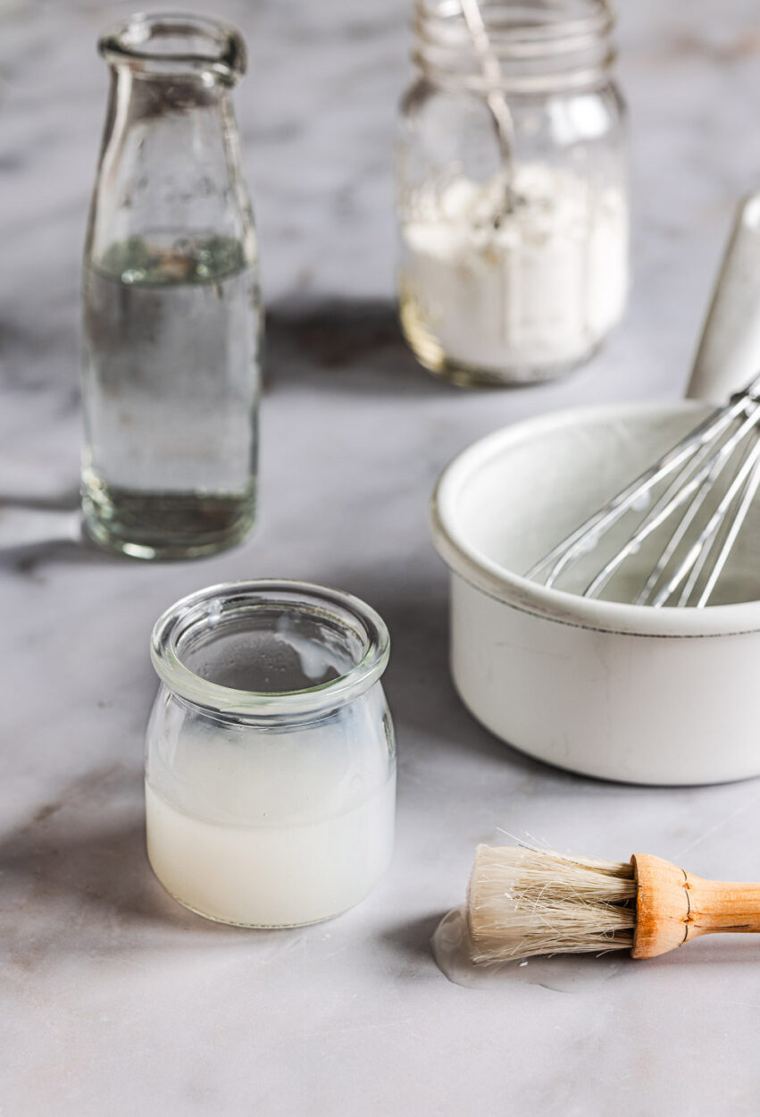 Zutaten für eine Glanzstreiche aus Stärke und Wasser und einem kleinen Glas mit der fertigen Glanzstreiche.