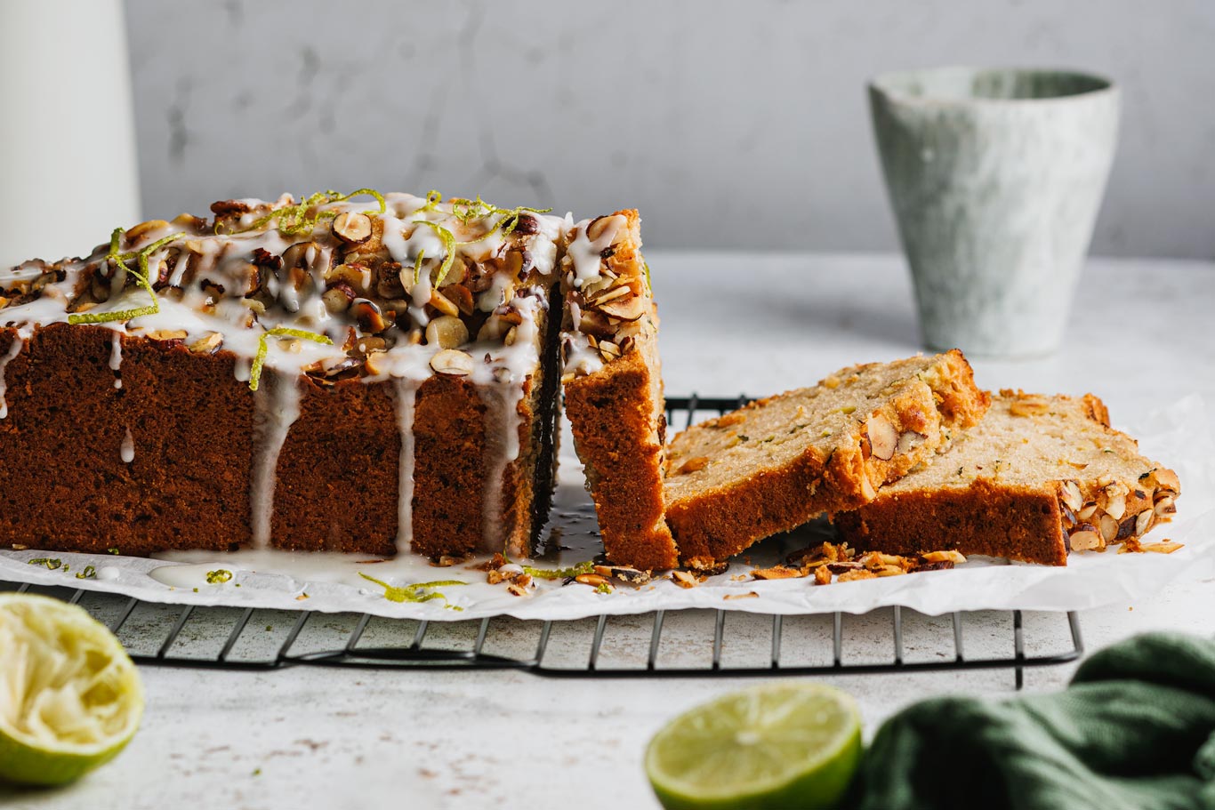 Zucchinikuchen auf einem Kuchengitter mit Zuckerguss und Limetten im Vordergrund.