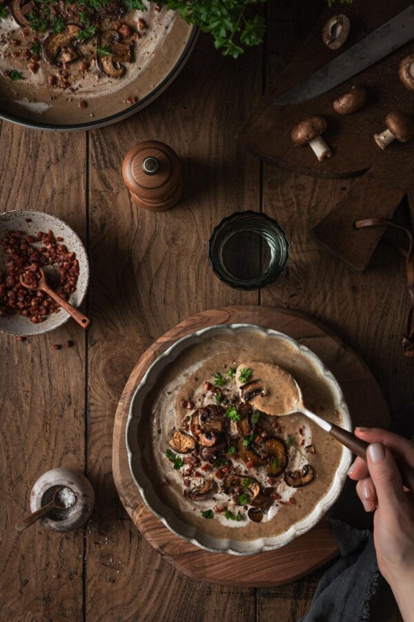Pilzrahmsuppe mit gebratenen Champignons, Speck und Petersilie.
