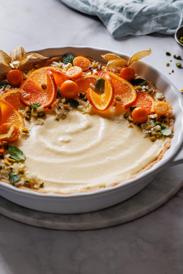 Orangentarte mit Mürbeteigboden und cremiger Füllung und einer Deko mit Orangen, Pistazien, weißer Schokolade und Physalis.